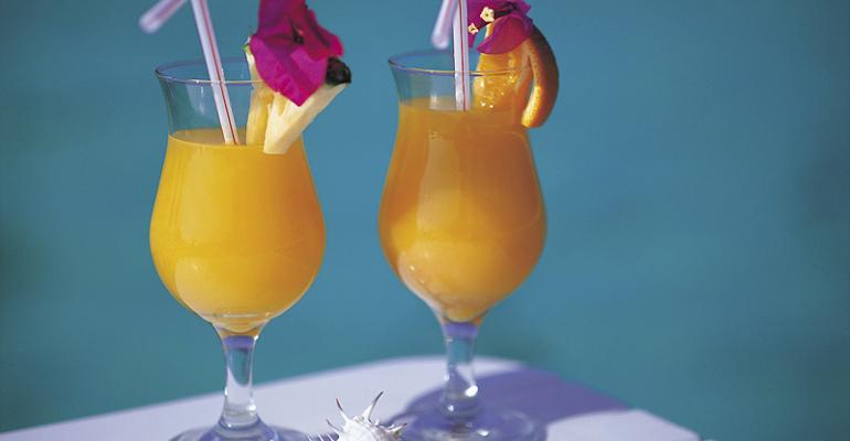 Two glasses of orange juice with pineapple slices and straws