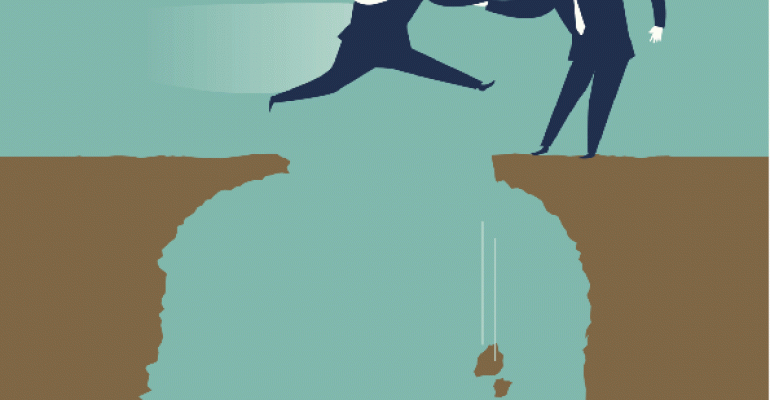 Businessman helping another businessman leap over crevasse