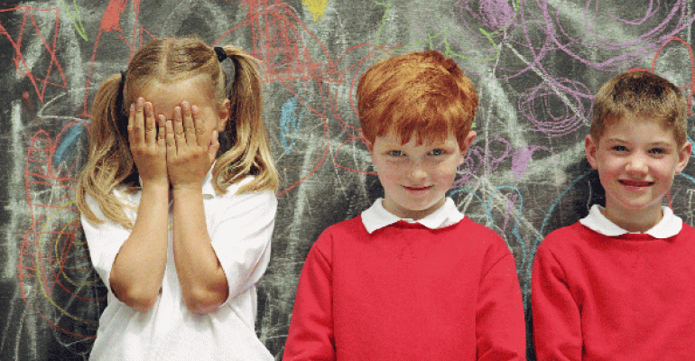 girl with hands over her face with two boys against chalkboard