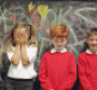 girl with hands over her face with two boys against chalkboard