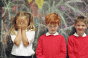 girl with hands over her face with two boys against chalkboard