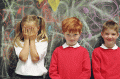 girl with hands over her face with two boys against chalkboard